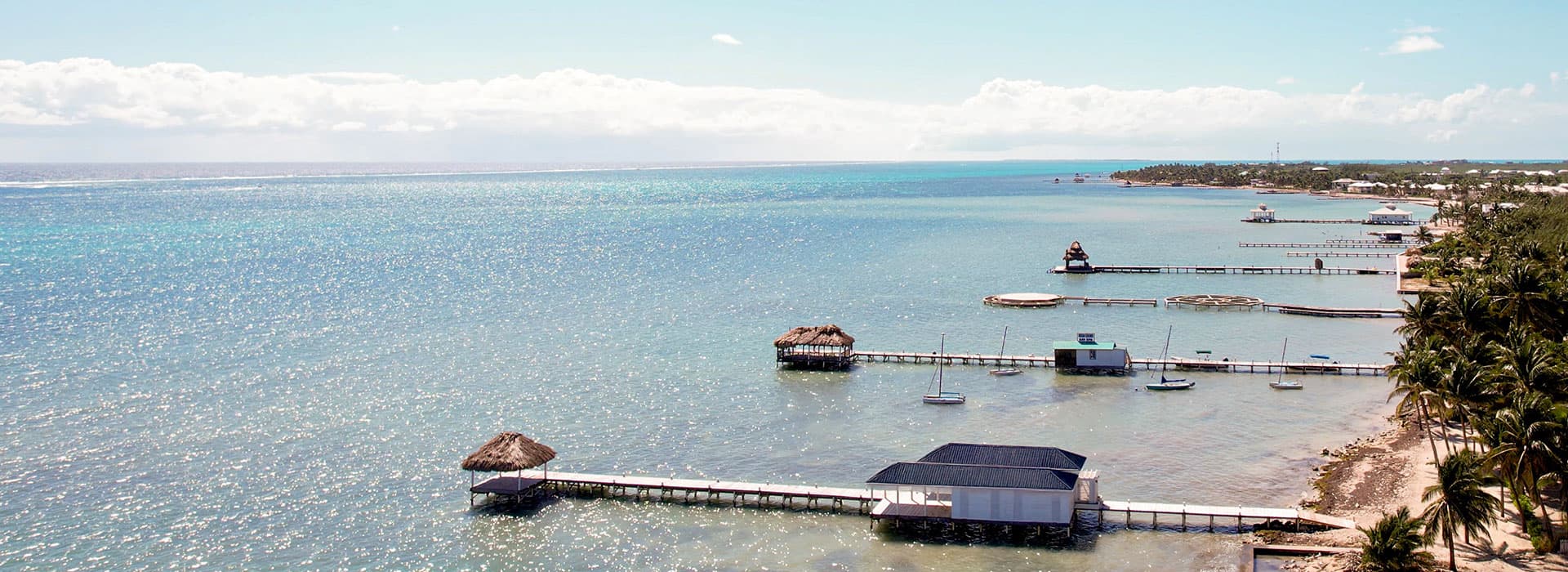 A panoramic view of a tranquil coastline with wooden piers and small boats on clear blue waters.