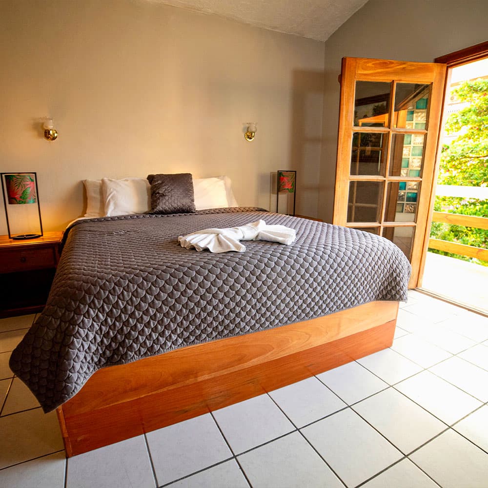 A neatly arranged bedroom featuring a gray quilted bedspread, decorative pillows, and open doors leading to a balcony.