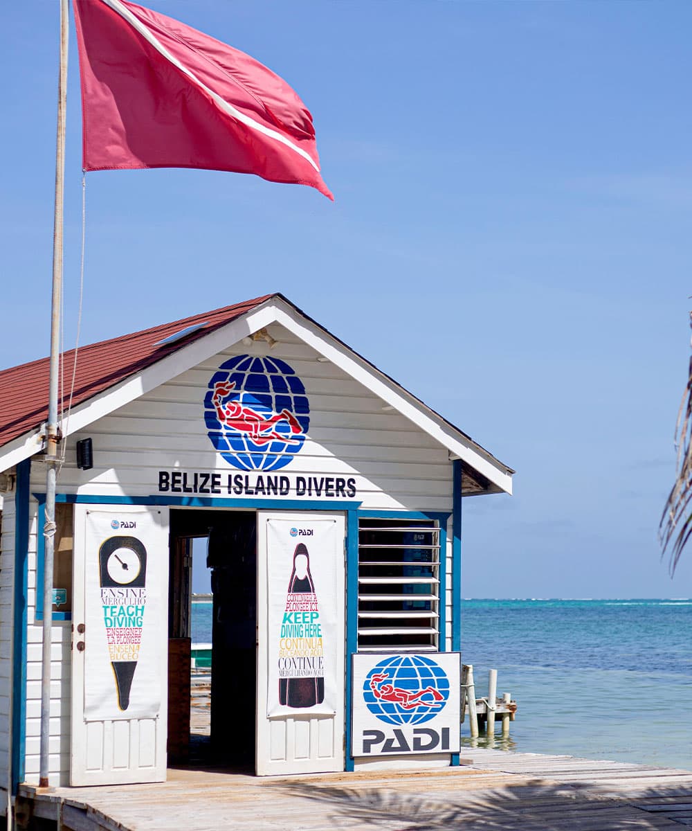 A dive shop in Belize features a red flag, blue and white signage, and scenic ocean views.
