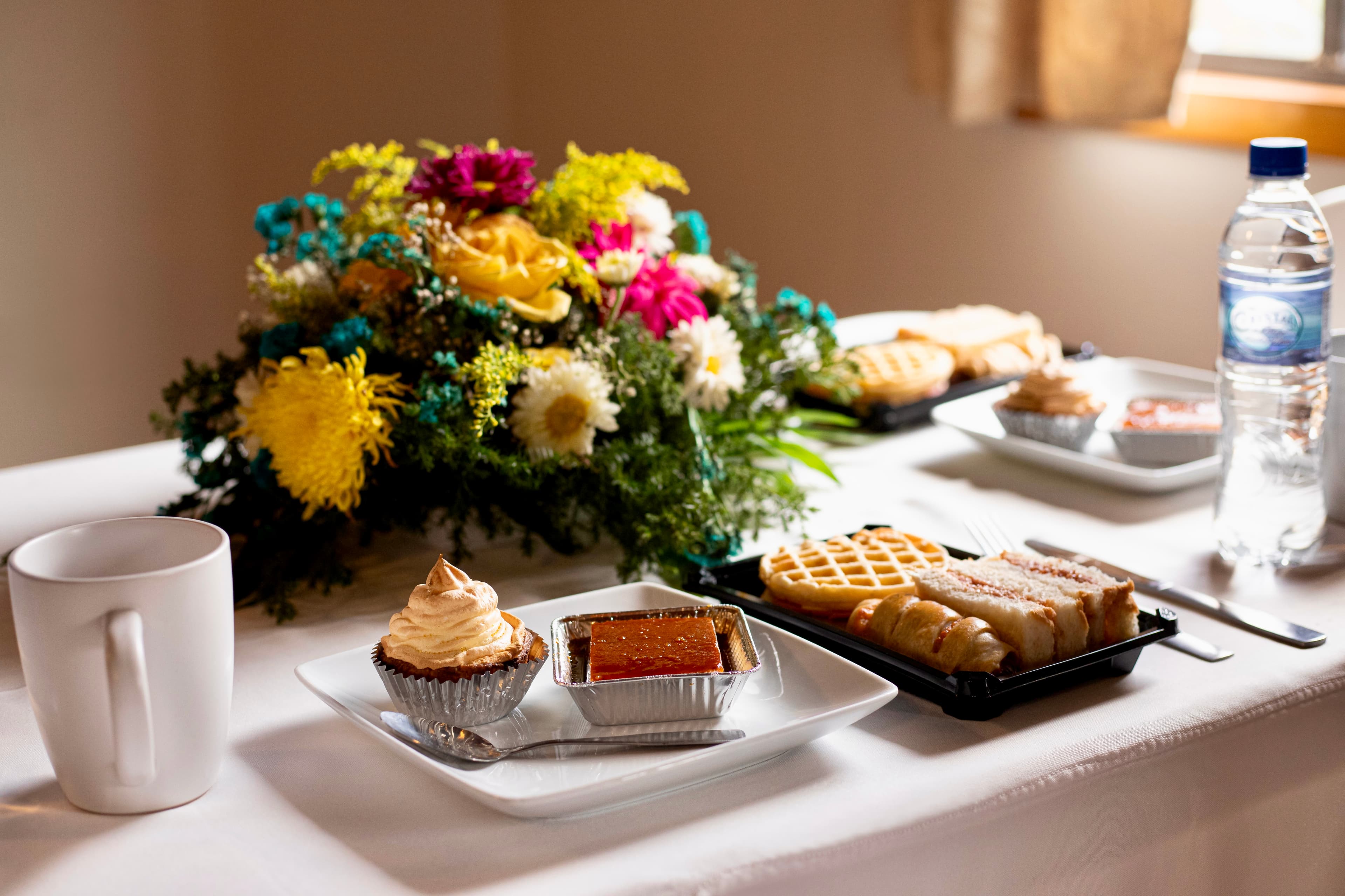 A table set with a floral arrangement, assorted desserts, and a cup.