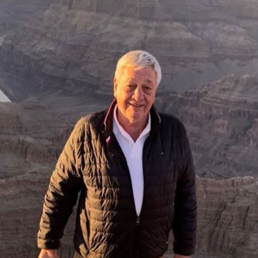 A smiling man stands against a scenic backdrop of rugged canyons.