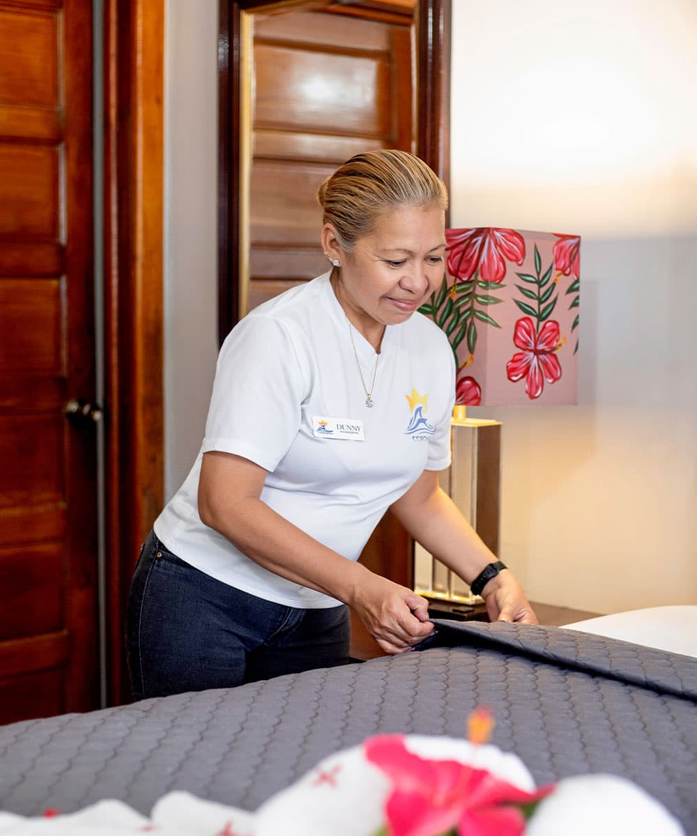 A woman adjusts a quilt on a bed in a warmly decorated room.