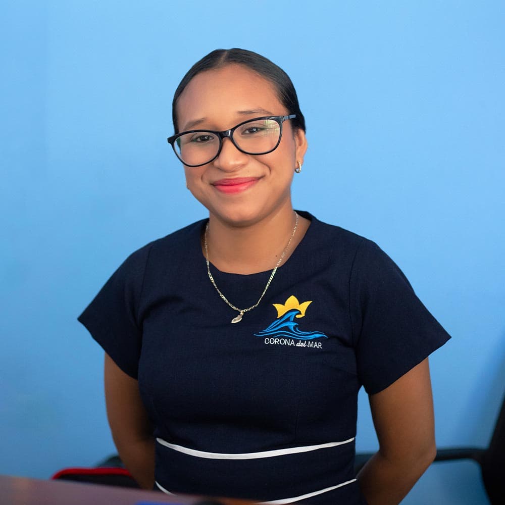 A smiling woman in a dark uniform with a logo sits in front of a blue background.