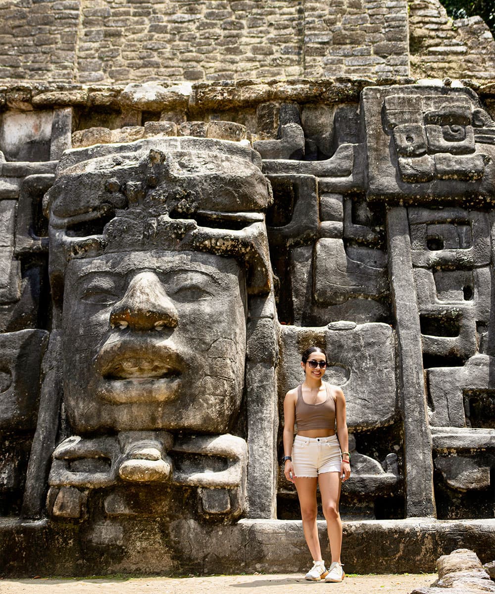 A person stands in front of a large stone carving depicting a face.