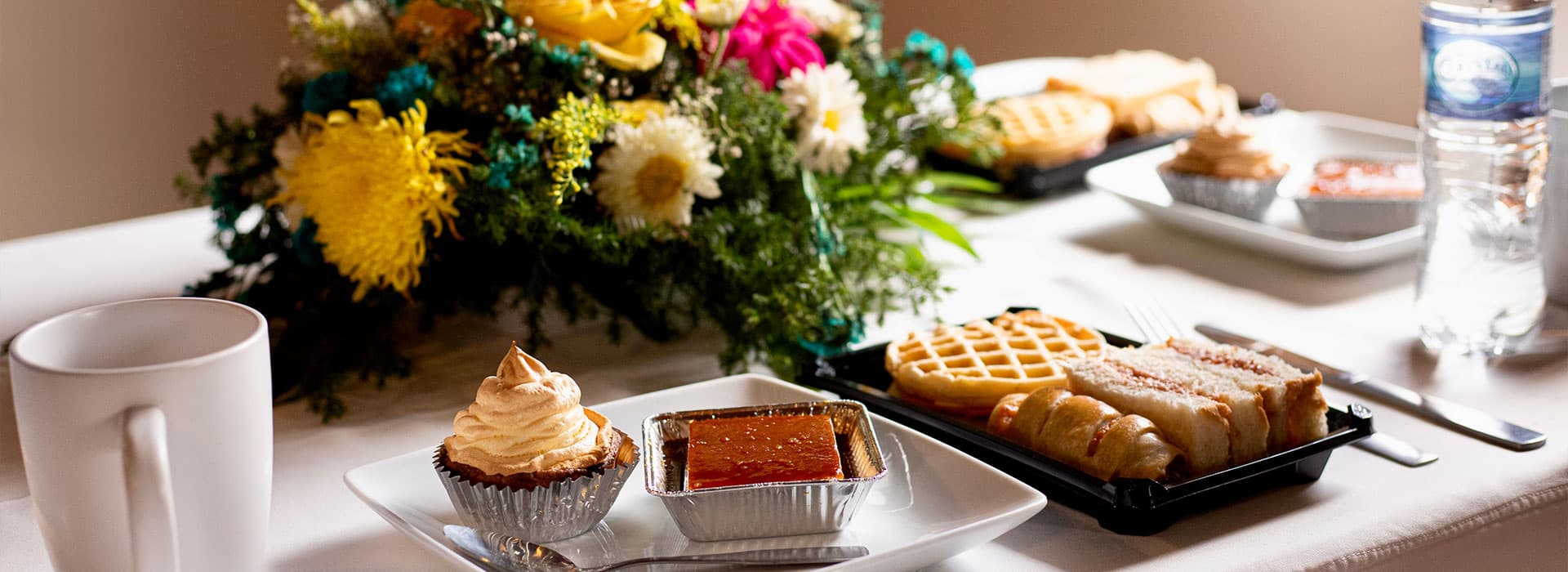 A table setting featuring various desserts, a cup, a water bottle, and a bouquet of flowers.